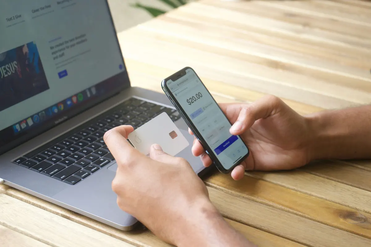 Hands using a smartphone beside a laptop