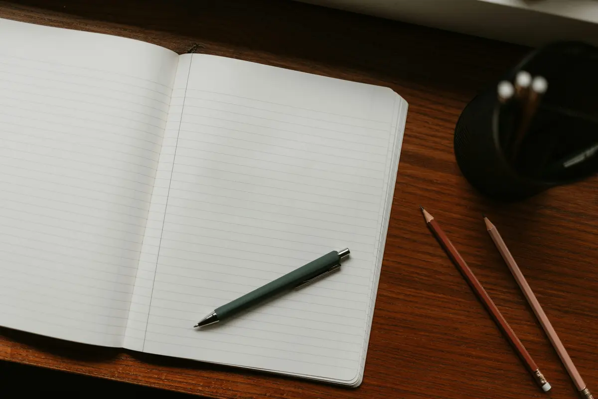 Open notebook with a pen and pencils on a wooden desk