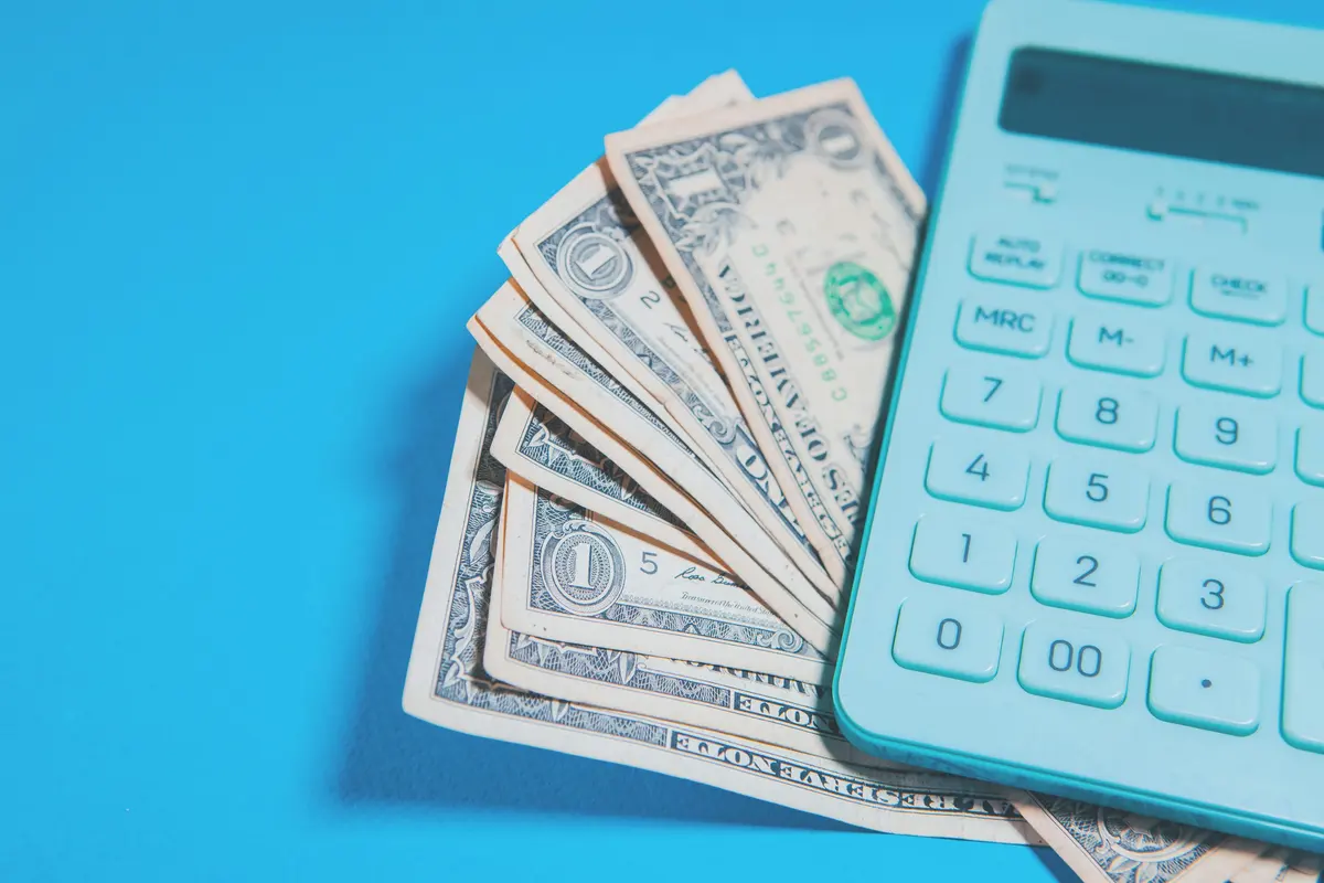 US dollar bills and a calculator on a blue surface